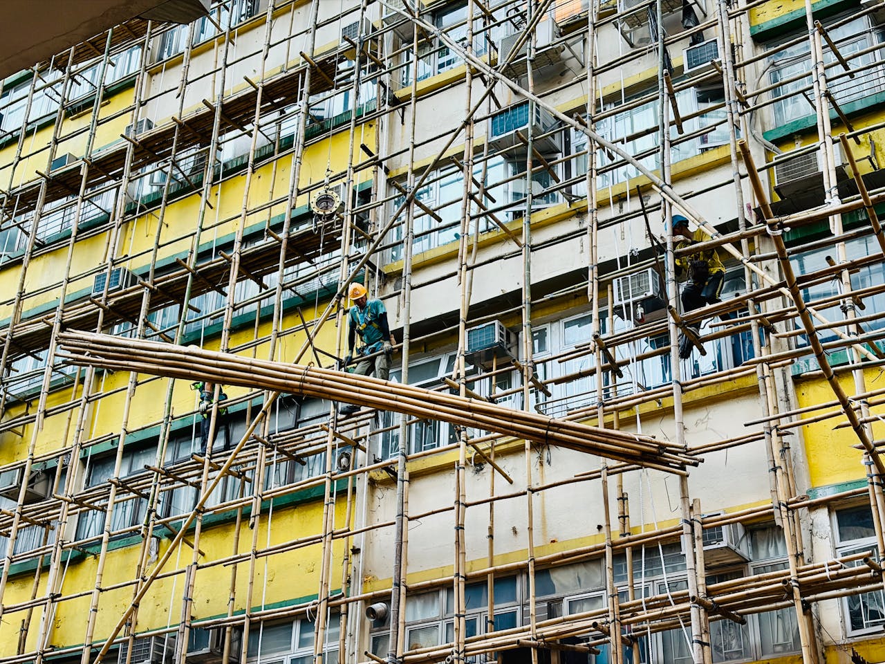 Builders working on bamboo scaffolding on a colorful building exterior.
